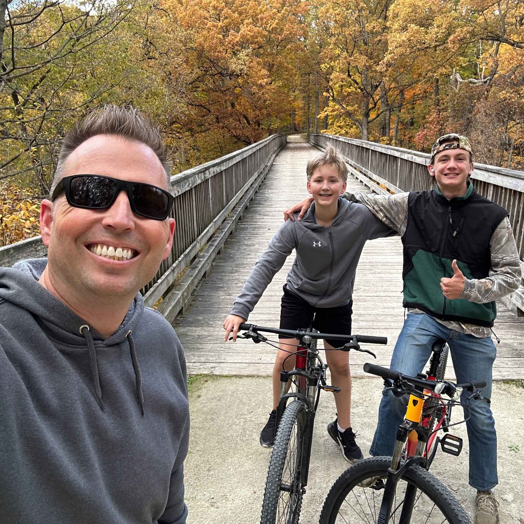 Selfie of 3 mountain bikers in front of the big bridge along the Goodenow Grove Nature Preserve trail